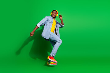 Fashionable young man enjoying music with headphones on a vibrant green background wearing trendy...