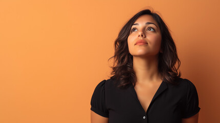 Latina Woman in Her 30s Looking Pensive with Arms Relaxed at Her Sides Against a Solid Pale Orange Background