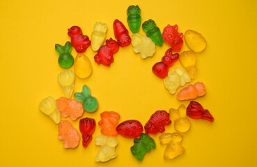 A festive wreath made of colorful gummy candies shaped like Easter bunnies, chicks, and carrots on a yellow background. A playful and bright holiday composition.