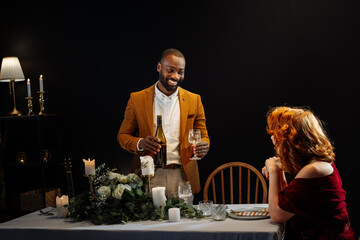 Man pouring wine for woman during romantic candlelit dinner