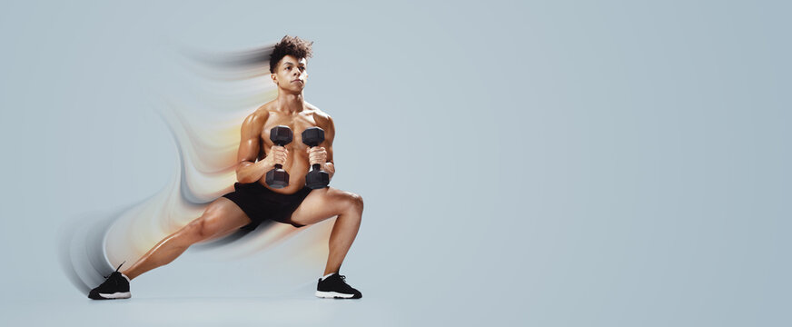 Athletic young man performing deep lunge while holding dumbbells, exercising on gray studio backdrop, full length. Strength and discipline, gym workout with weights concept