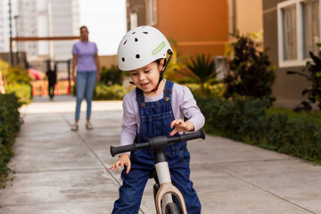Mamá con hija enseñando a montar bicicleta de equilibrio al aire libre.
