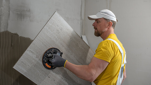 Tiling with large format tiles. A tiler placing a tile held by a tile suction cup.
