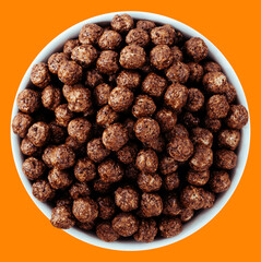 Bowl of chocolate cereal balls on an orange background. Crunchy breakfast option made of cocoa-flavored puffed grains.