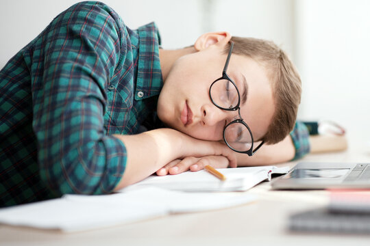 Exhausted school boy in glasses sleeping at desk, got tired from studying, home interior, side view, copy space