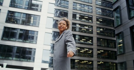 A young African-American woman wearing headphones, dressed in a business jacket over a crop top,...