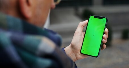 Gray-haired man using mobile phone with green screen swiping his finger across the screen to the side, unrecognizable person, top view from behind the man's shoulder. Video in 4k, red komodo