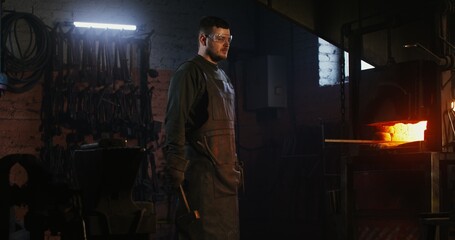 A blacksmith dressed in a hazmat suit turns his head and looks straight into the camera as he...