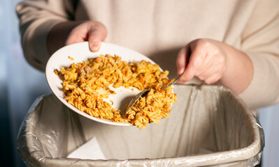 Woman holding white plate with food leftovers and throwing away food into garbage bin trash. Compost from leftover food. Environmentally responsible, reducing pollution.