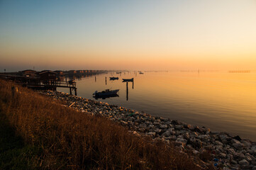 Obraz premium winter sunset over the Scardovari lagoon with fishing boats and cabins inside the delta of the river Po, Porto Tolle, Veneto