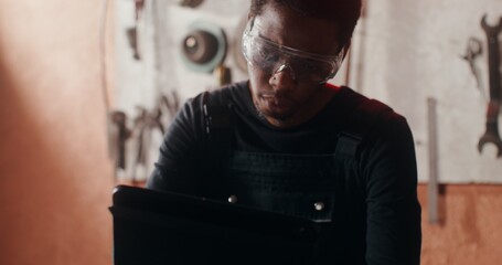 A young African-American man in goggles with a serious look draws a sketch of a product, using a...