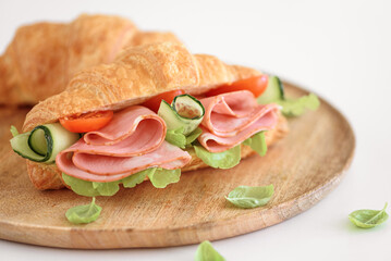 Ham and Cheese Croissant Sandwich on wooden plate on white table. Healthy breakfast.