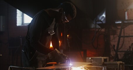 A man of African American appearance, dressed in work clothes and goggles with a concentrated look,...