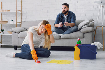 Cleaning, duties and sexism at home. Man has fun with video games, tired wife clings to her head...