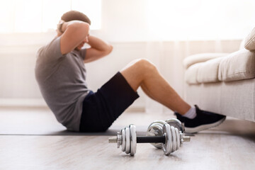 Guy does exercises for abs, shove his legs under couch in living room in daylight, at interior....