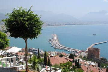 Scenic coastal view from a hill overlooking a marina and a historic fortress. The turquoise sea,...