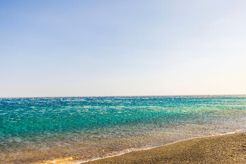 Strong katabatic wind from mountains pushes Aegean sea waves back from shore, creating reverse flow effect under clear sky. Greece.