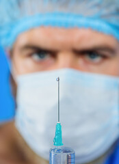 Syringe with needle, closeup. Male doctor in surgical mask preparing syringe with needle for...