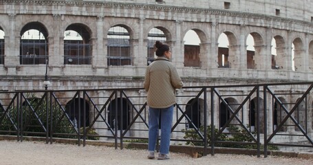 A young warmly dressed Caucasian woman smiles as she takes in the sights of Rome from an observation deck near the Coliseum. Video in 4k, red komodo.
