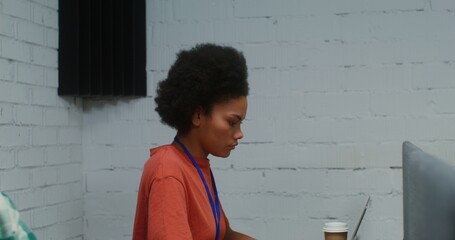 A young beautiful African American woman uses a laptop, working at the same desk with a partition in front of a young Asian man, video from the side. 4K video, red komodo