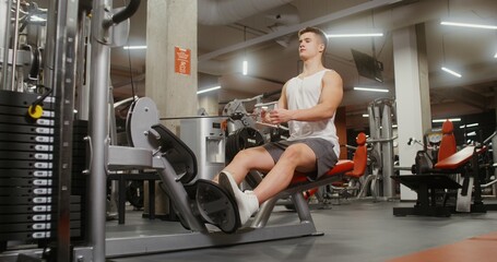 Fototapeta premium A healthy young man of European appearance is engaged in an exercise machine, shaking his chest muscles, lifting weights with his hands, sitting on a bench