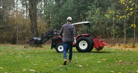 Young male farmer getting ready to start work in the field on an autumn day, getting into a modern agricultural tractor and starting it