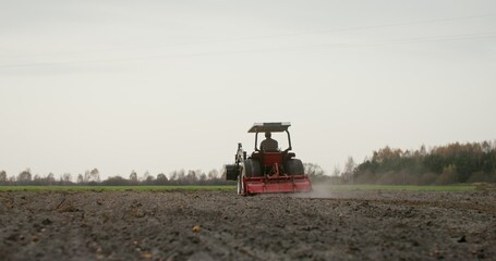 Obraz premium A young male farmer plows a field on a small farm tractor with a plow on an autumn day. Preparing the soil for planting winter crops