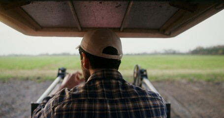 Close-up, rear view from the tractor cabin to a male farmer, driving an agricultural tractor while...
