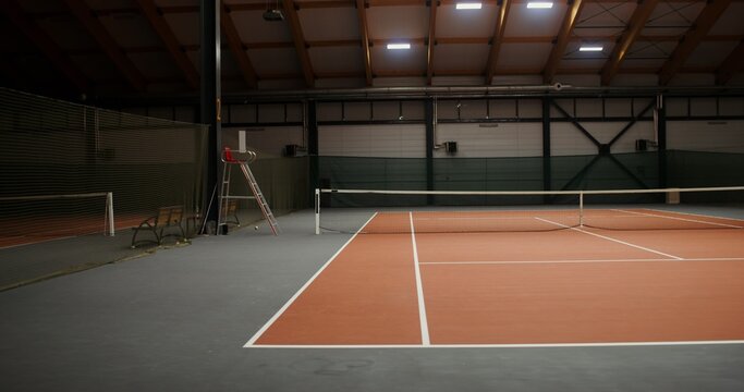 An empty tennis court with a rubberized orange covering on the floor and a net stretched in the middle, the video gradually transitions from one edge of the cort to the other, no people in the video