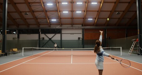 Obraz premium Young athletes - a man and a woman of European appearance play tennis in a large hall alone, throwing the ball with a racket over the net to each other