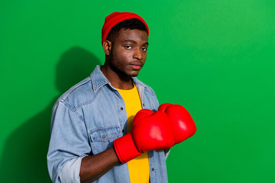 Stylish young man wearing casual clothing and red boxing gloves against a bright vibrant green background - Powered by Adobe