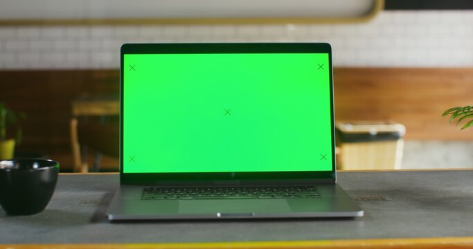 open laptop with a green screen stands on a table in coffee shop open laptop with a green screen stands on a table in a coffee shop, close-up. There are no people in the frame. Chrome key, copy space
