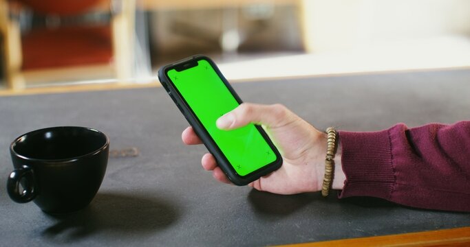 A man uses a phone with a green screen while sitting at a table. Male hand close-up, copy space, chroma key. - Powered by Adobe