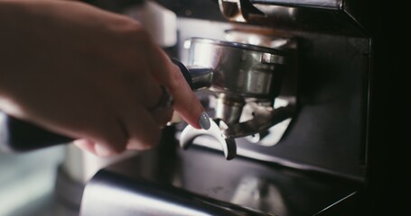 Freshly ground coffee is poured from a professional coffee grinder into a container, which is taken by a woman's hand. Close-up, no face in the frame