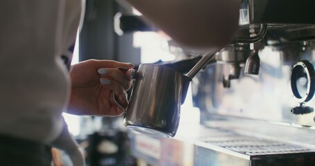 A woman pours warm cream into a decanter from a coffee machine. Close-up, no face in the frame,...