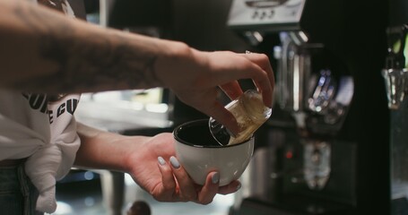 Young woman barista with tattoos on her arms makes coffee in a coffee shop, close-up, only female hands with a mug in the frame, the woman's face is not visible
