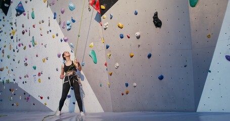 A young woman pulls on a safety rope for a man descending from a climbing wall while standing at...