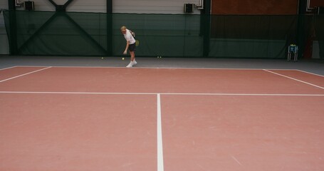 A young male tennis player of European appearance prepares to throw a tennis ball, stuffing it with his hand from the floor covering, then makes a strong hit with a racket