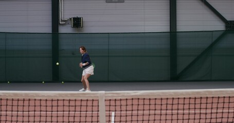 A young woman athlete plays tennis, deftly repulsing blow after blow with a racket. Indoor tennis...