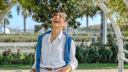 A young brunette businesswoman in a tree-filled park on a spring day, smiling at the camera