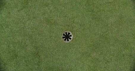 An overhead view of a golf course set on artificial turf. The golf ball rolls up to the hole and spins around its circumference