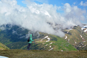 A girl in a green jacket stopped on a mountain and looked at the mountain and cloud landscape in the distance