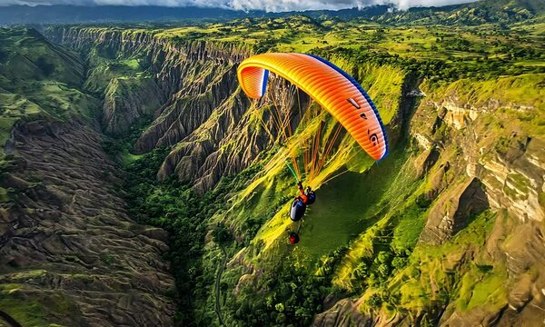 A paragliding adventure over lush green mountains with dramatic cliffs and a clear blue sky