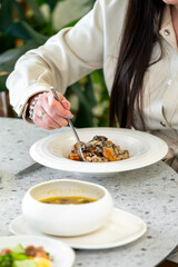 A close-up of a person enjoying a gourmet meal in a modern restaurant. The plate features a stylish dish with mushrooms, and a bowl of soup is visible on the table.