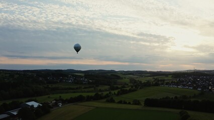Drone shot of a hot air balloon in the sky flying over neat village houses nestled in a green...