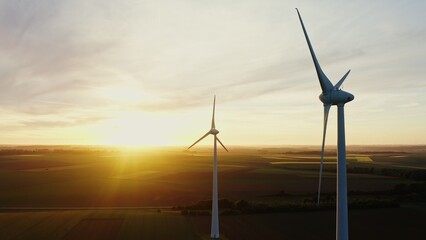 Wind turbines against the backdrop of the sun setting over the multi-colored fields. Wind farm at...