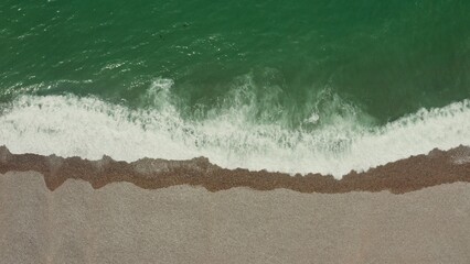 Top view of the sea shore. Emerald water with foam washes a shallow pebble beach, drone video.