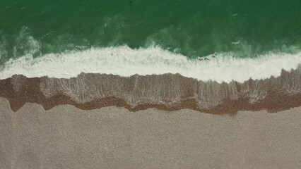 Top view of the sea shore. Emerald water with foam washes a shallow pebble beach, drone video.