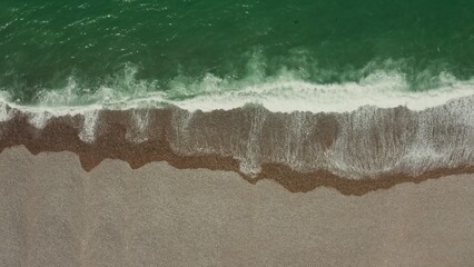 Top view of the sea shore. Emerald water washes the pebbly shore, leaving foamy patterns, drone video.