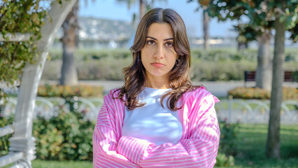 Naklejka premium A young brunette businesswoman in a park full of trees on a spring day looks at the camera with facial expressions showing she is sad